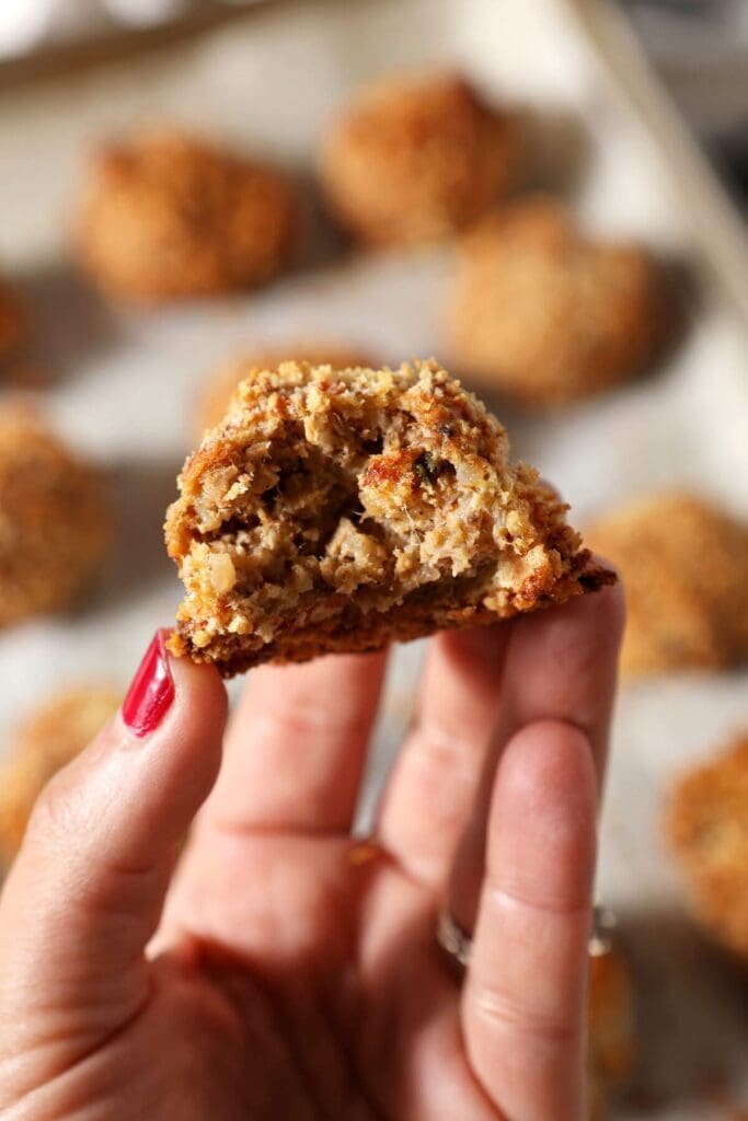 A bitten-into boudin ball held in a hand above a sheet pan of baked boudin balls