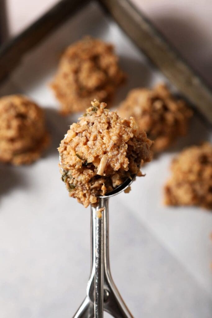 The boudin mixture in a cookie scoop held above a parchment-lined sheet pan