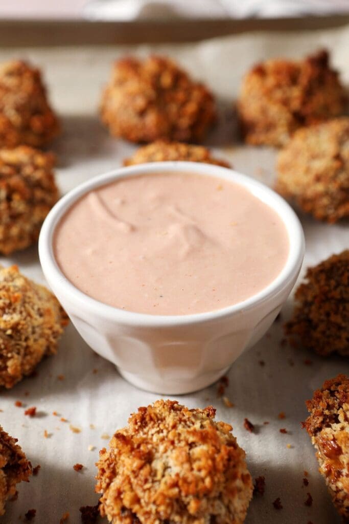 A Louisiana dipping sauce in a white bowl surrounded by homemade boudin balls