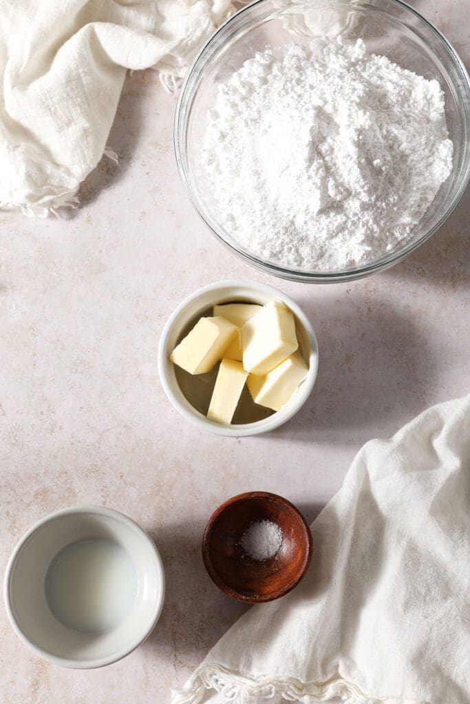 Ingredients to make brown butter frosting in bowls on a brown surface with two white linens