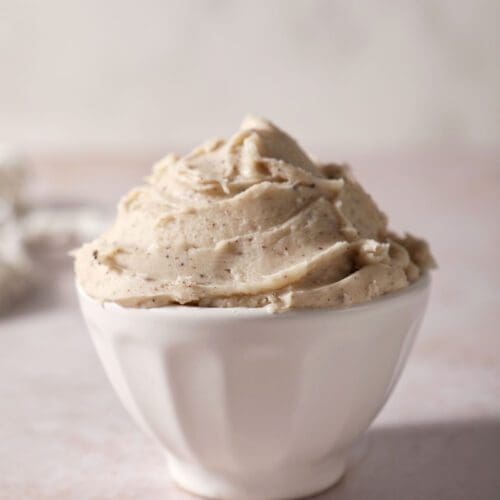 A white bowl of brown butter frosting on a brown surface