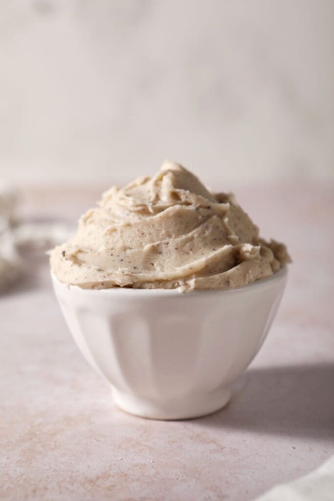 A white bowl of brown butter frosting on a brown surface