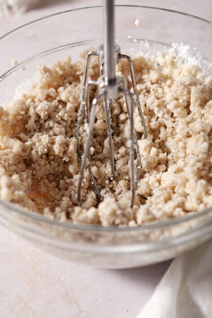 A hand mixer blends ingredients together to make a brown butter icing in a glass bowl