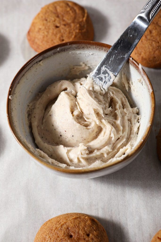 A butter knife swirls a bowl of browned butter frosting surrounded by cookies