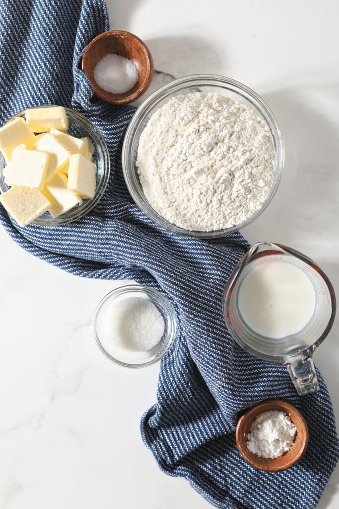 Ingredients in bowls to make a buttermilk pie crust on marble with a blue striped towel