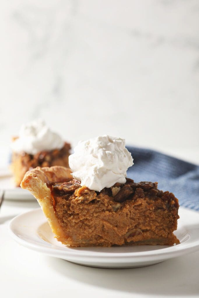 Close up of a tall piece of pumpkin pie topped with whipped cream on a white plate