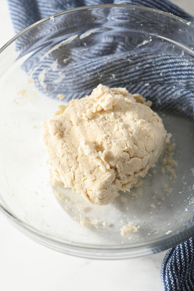 A round of pie crust in a glass bowl with a blue striped towel