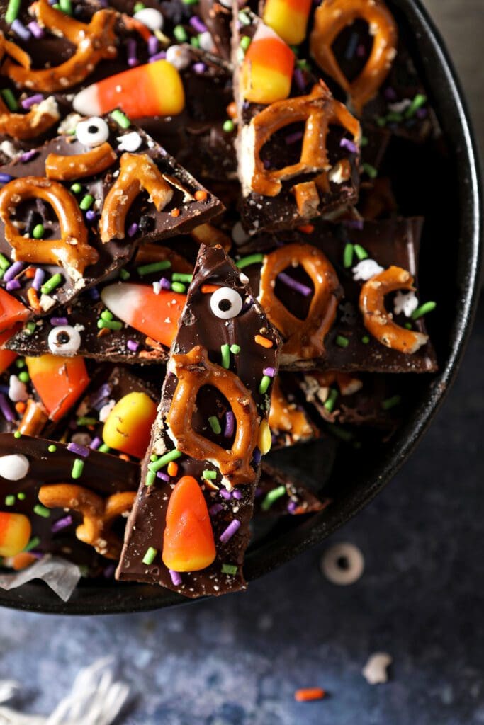 sliced halloween bark with candy eyeballs, pretzels, sprinkles and candy corn in a black bowl on a blue surface