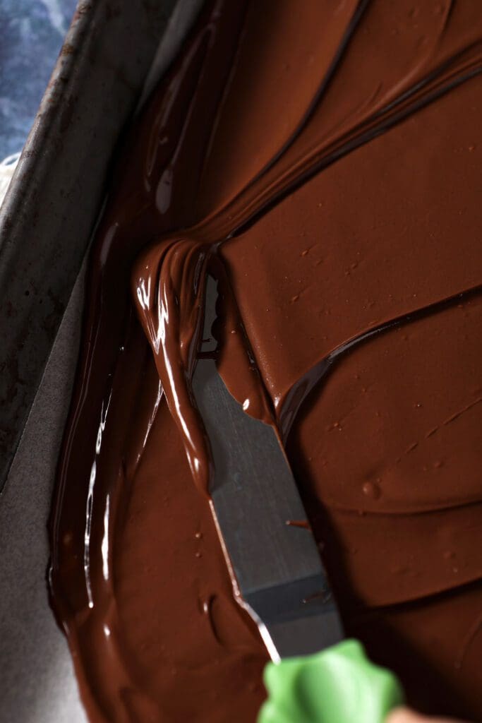 an offset spatula spreads melted chocolate onto a sheet pan