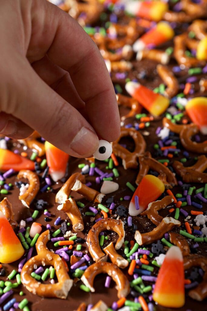 a hand adds a candy eyeball sprinkle to finish halloween bark before chilling