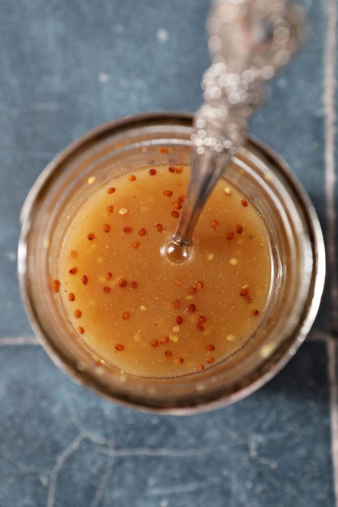 Bacon vinaigrette from above in a mason jar with a spoon on a dark blue tiled surface