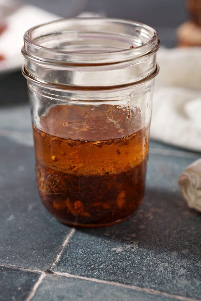 Ingredients for warm bacon vinaigrette in a mason jar on a blue tiled surface before mixing