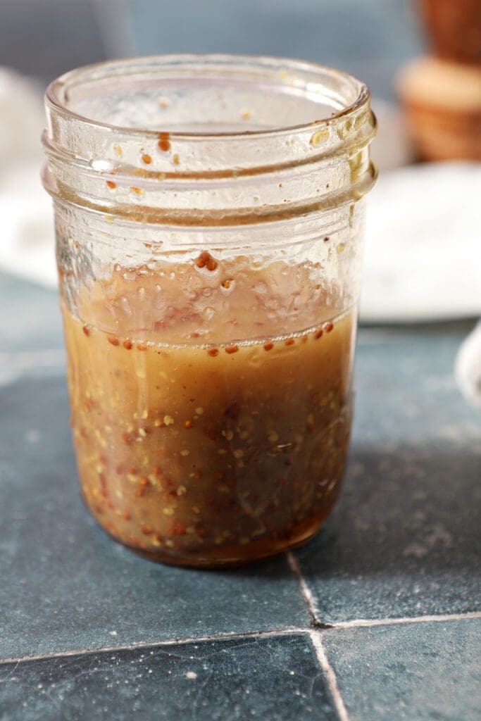 Ingredients for warm bacon vinaigrette in a mason jar on a blue tiled surface after mixing