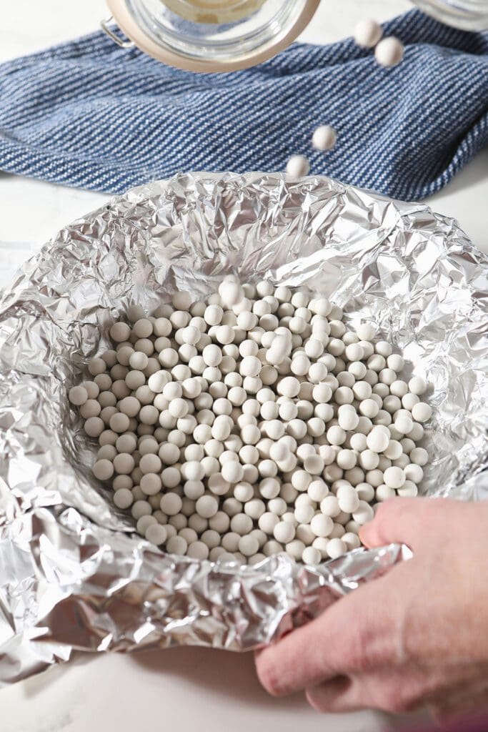 Ceramic pie weights are poured into a pie plate lined with foil