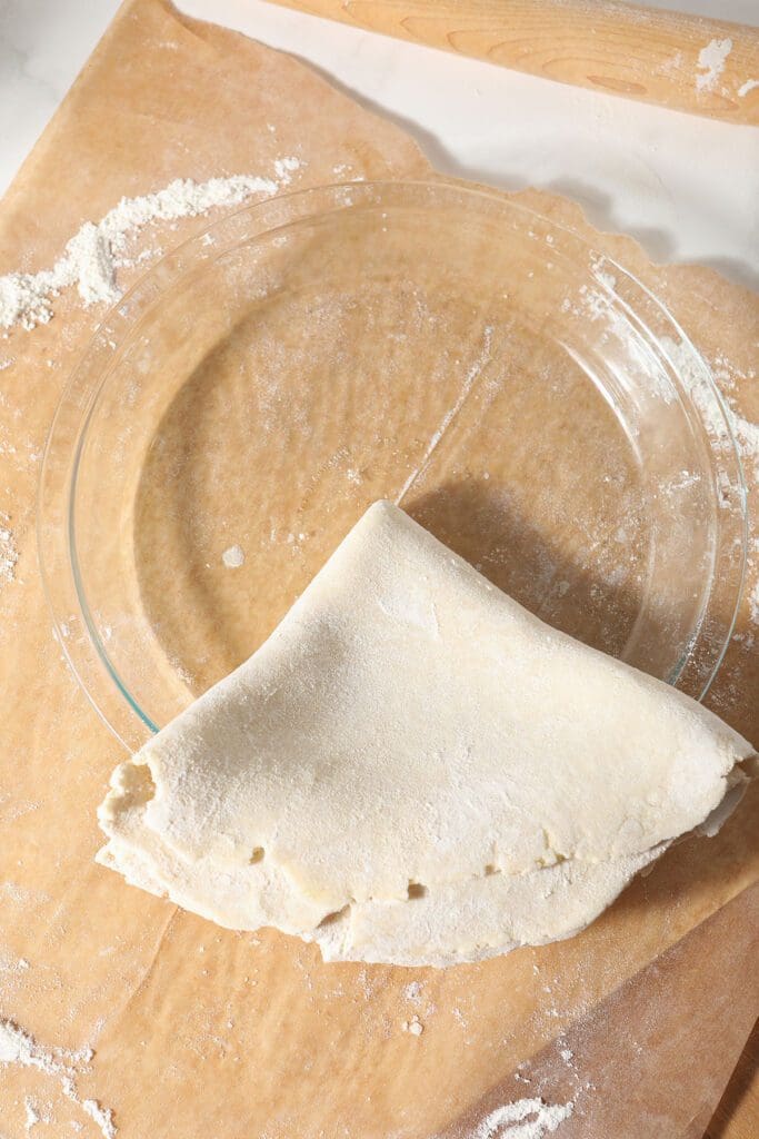 Pie crust, folded into fourths, placed on a glass pie plate before unfolding