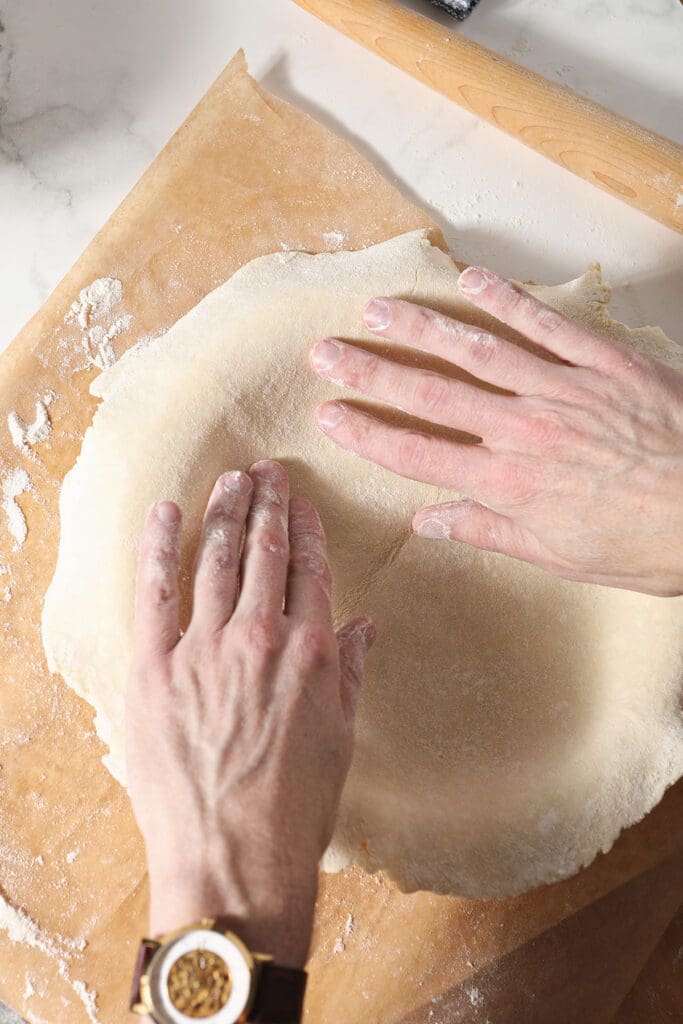 A set of hands presses a round of pie crust into a pie plate