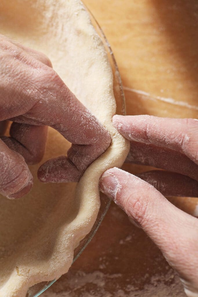 A pair of hands crimps the edges of a pie crust