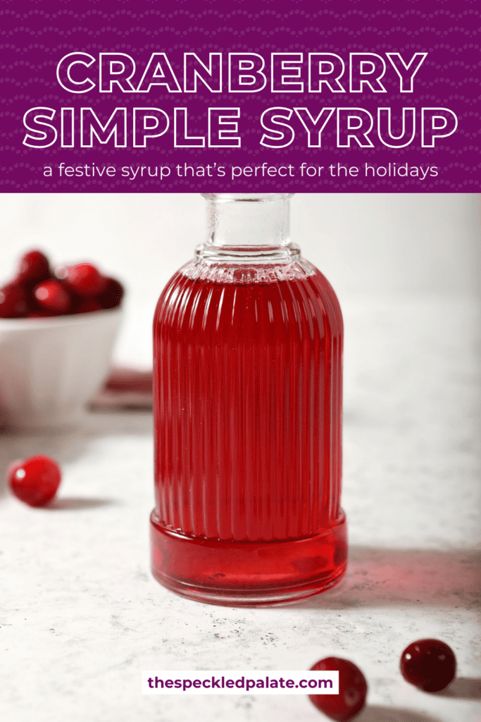 A ribbed glass jar of cranberry simple syrup with cranberries around it on marble with the text cranberry simple syrup a festive syrup that's perfect for the holidays