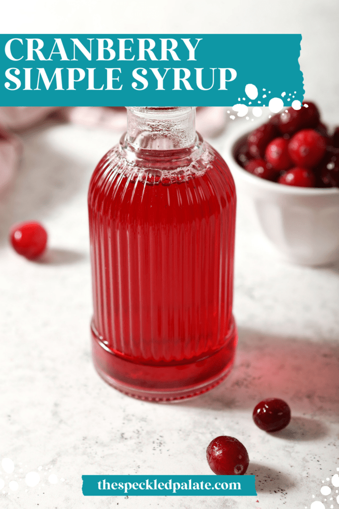 A ribbed glass jar of cranberry simple syrup with cranberries around it on marble with the text cranberry simple syrup