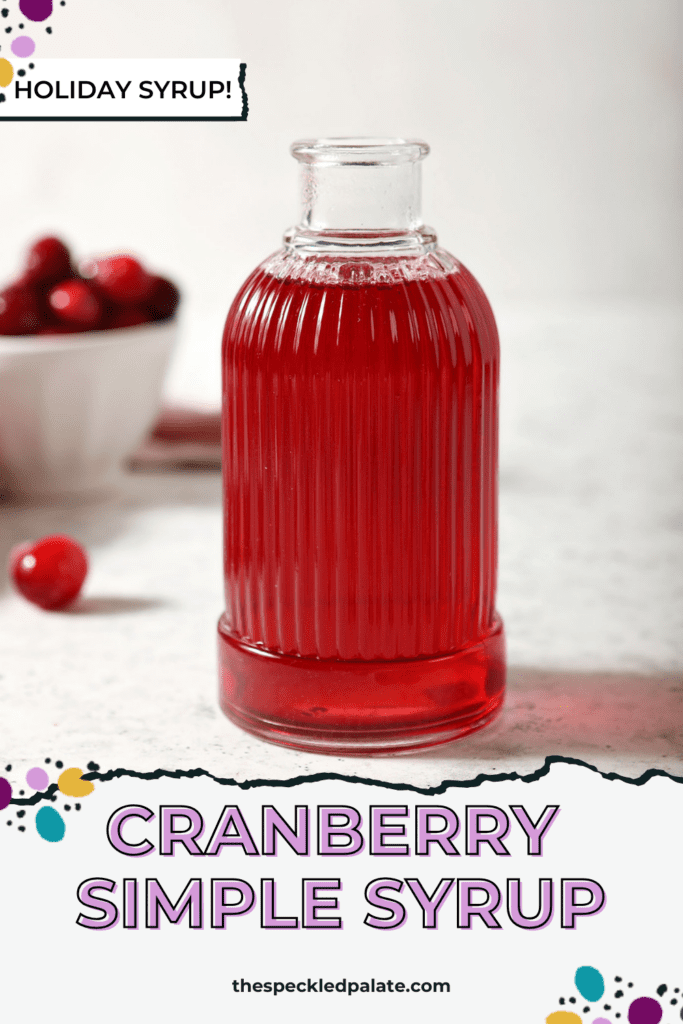 A ribbed glass jar of cranberry simple syrup with cranberries around it on marble with the text cranberry simple syrup