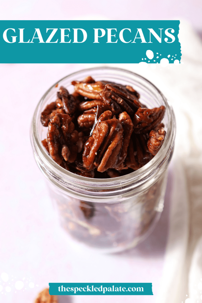 A mason jar of glazed pecans on a pink surface next to a white linen with the text glazed pecans