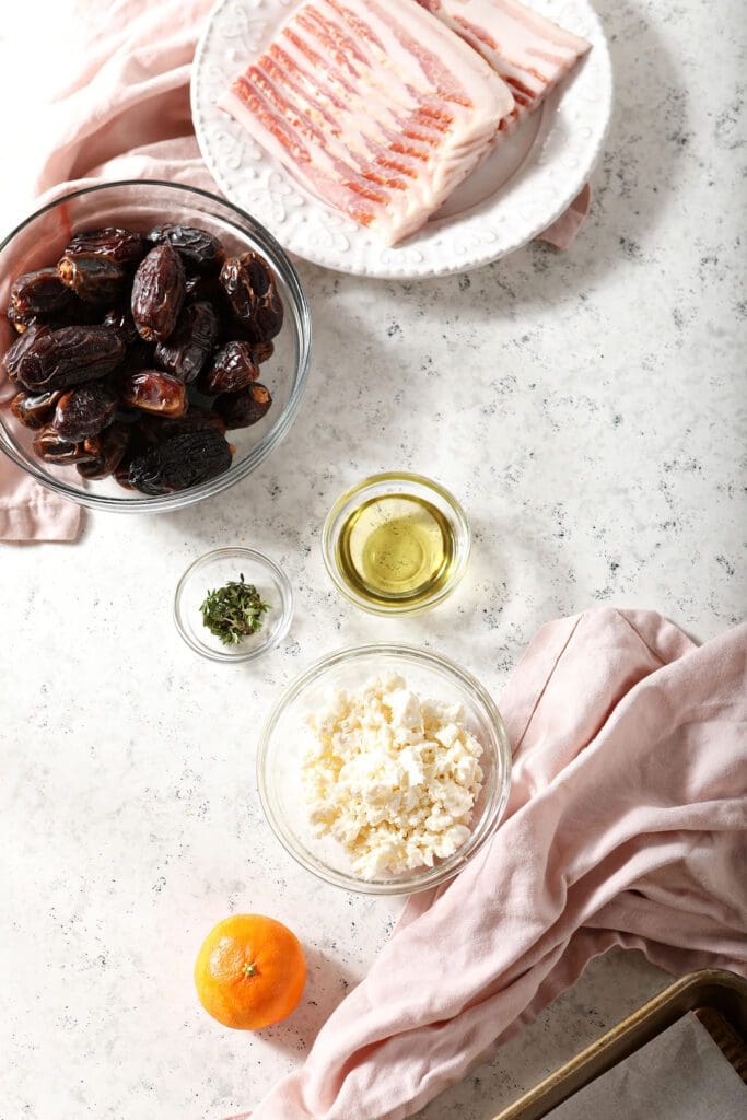 Ingredients in bowls to make stuffed dates with bacon on a textured white surface with pink linens