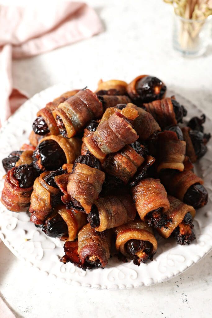 A platter of bacon wrapped dates with a pink linen and a container of toothpicks