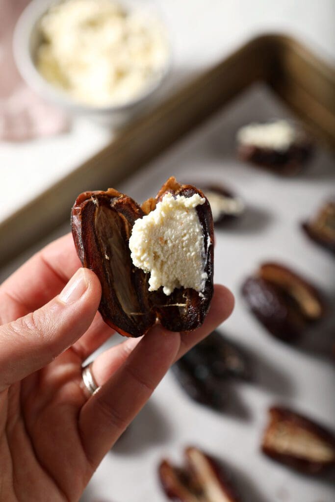 A pitted date filled with a feta filling in a hand above a sheet pan