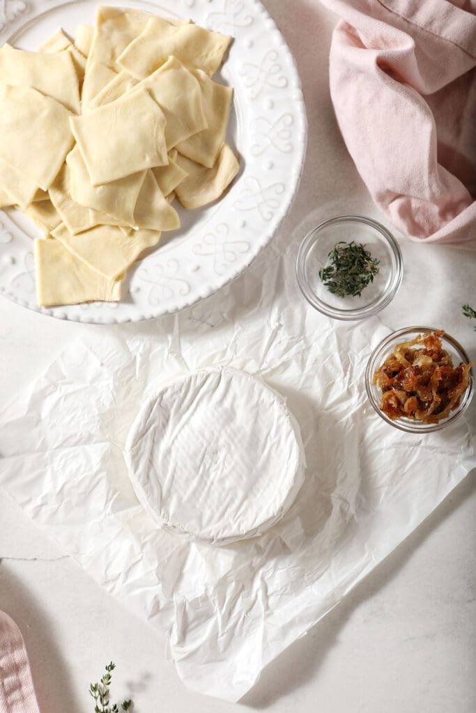 Ingredients to make baked brie bites on a marble surface with pink linens