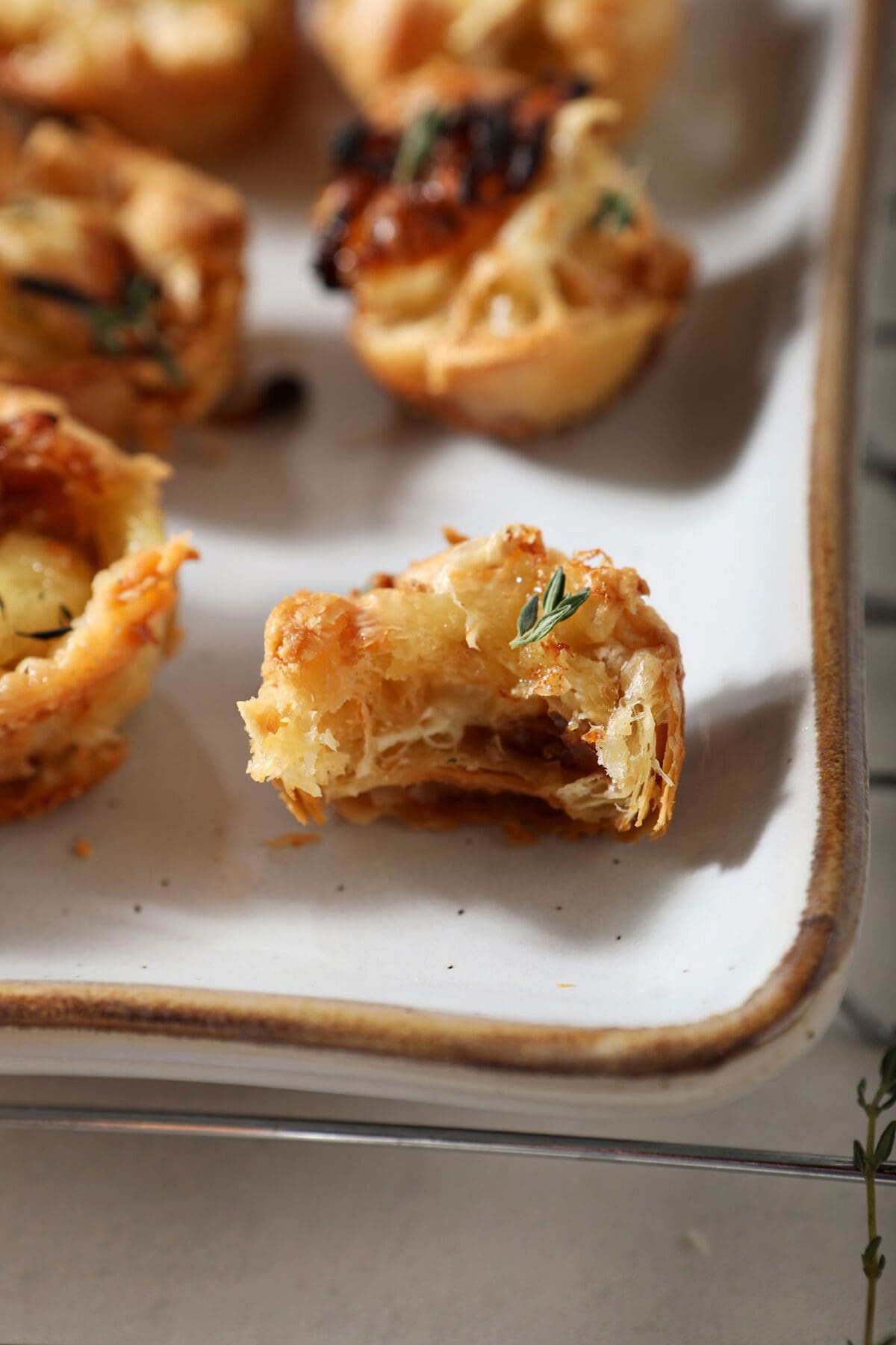 A bitten-into brie bite sits on a white platter next to other brie bites