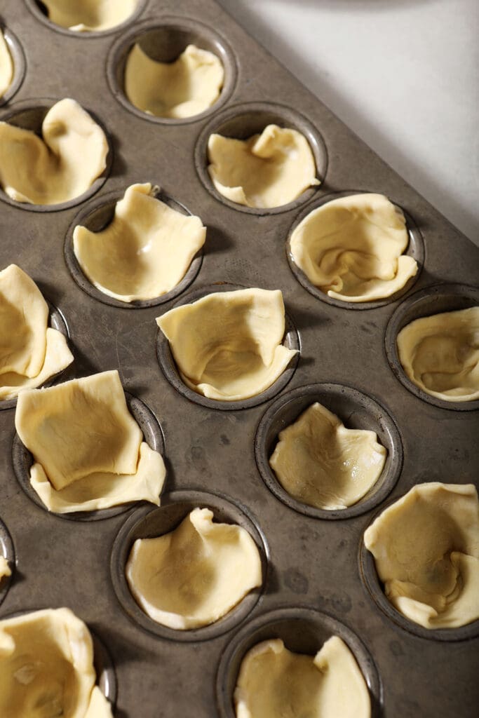 Puff pastry lines the divots of a mini muffin tin