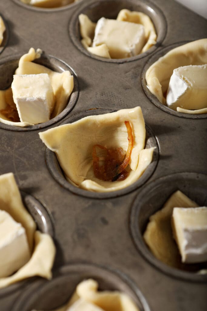 Caramelized onion inside a square of puff pastry in a mini muffin tin