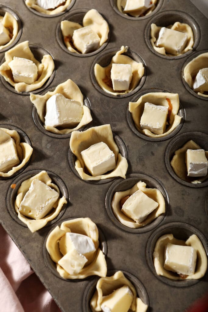 Brie squares on top of puff pastry on a mini muffin tin