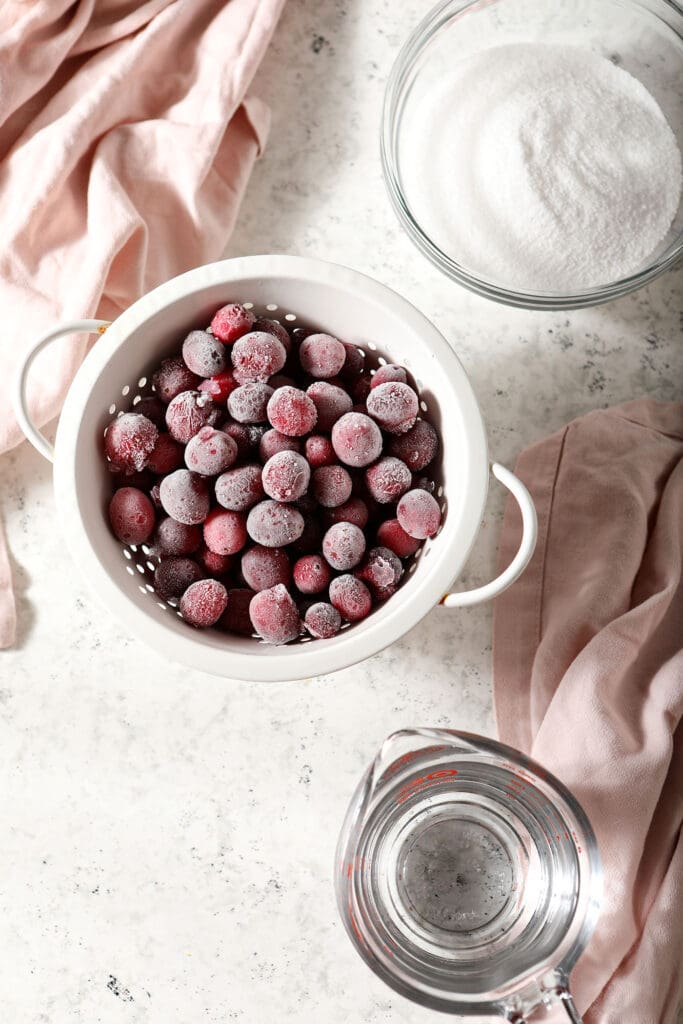 Ingredients to make cranberry simple syrup in bowls on marble with pink linen