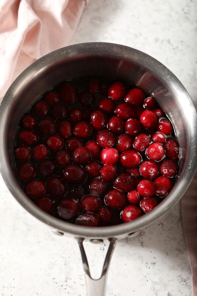 A saucepan with cranberries and liquid on marble