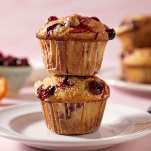 A stack of two Cranberry Muffins on a white plate, surrounded by cranberries and orange slices