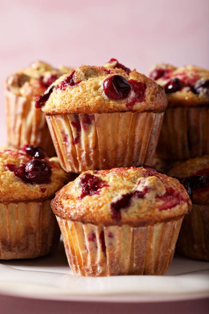 A white plate holds several Cranberry Muffins stacked on top of each other