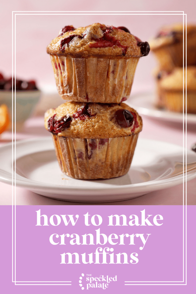 A stack of two Cranberry Muffins on a white plate, surrounded by cranberries and orange slices with the text how to make cranberry muffins