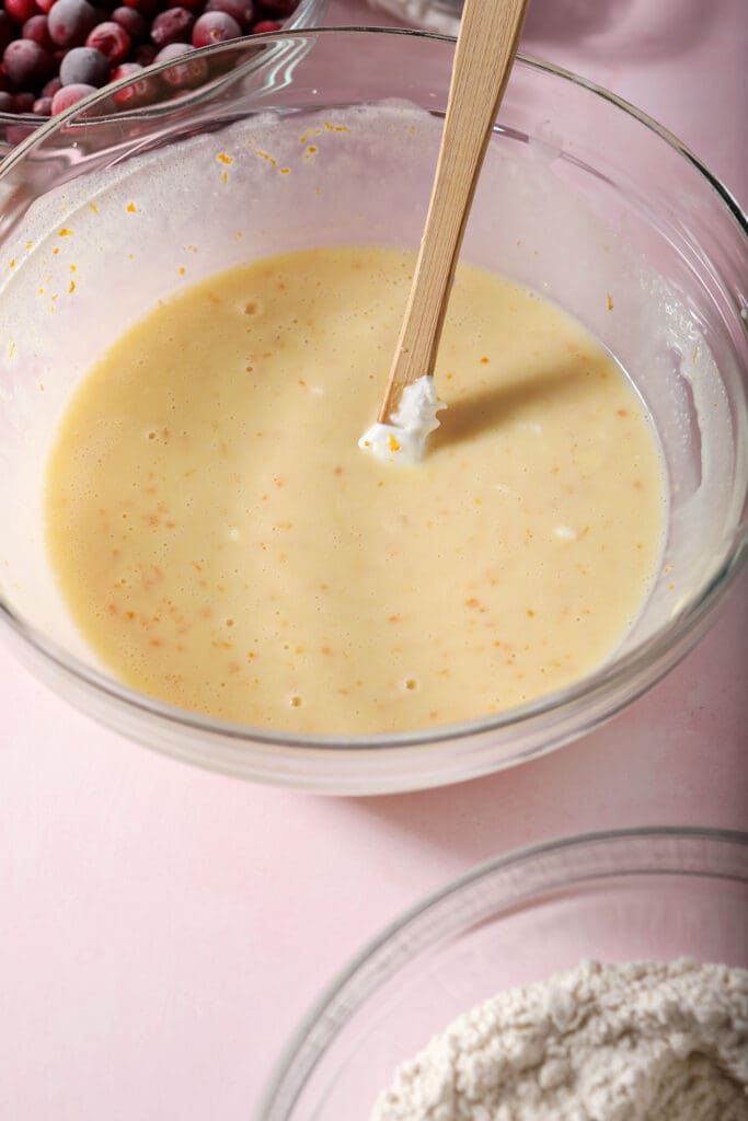 A small rubber spatula in a bowl full of an orange-yellow liquid on a pink surface