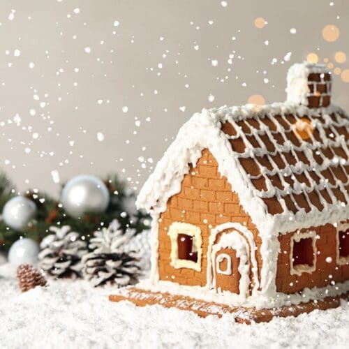 a beautiful gingerbread house decorated with white icing on snow with sparkles