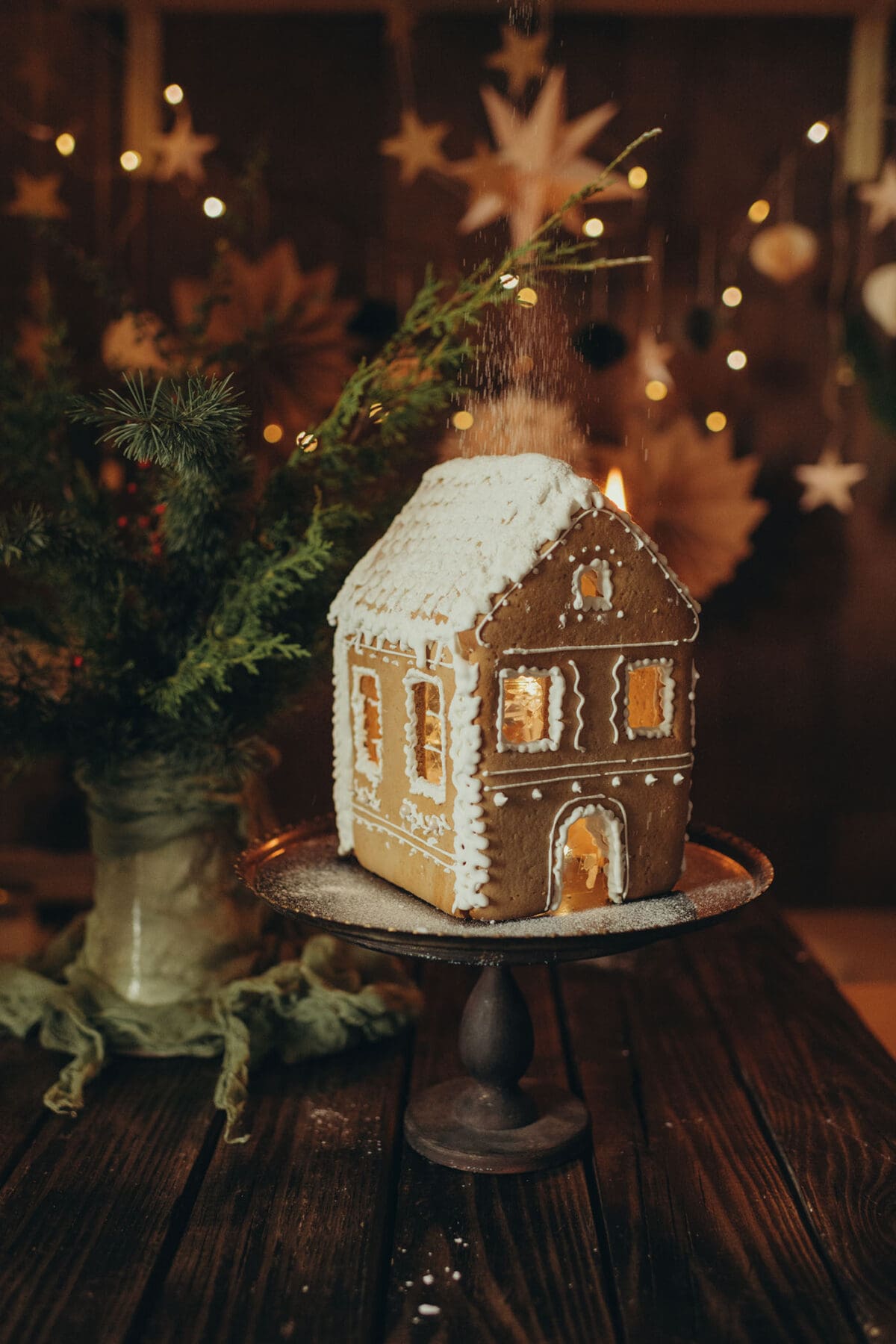 a skillfully decorated gingerbread house on a platform in front of a christmas tree