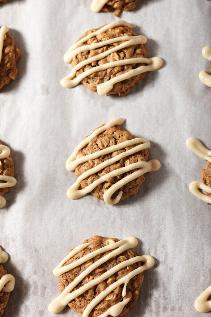 Cinnamon Oatmeal Cookies drizzled with a with Maple Cream Cheese Glaze on a parchment-lined sheet pan