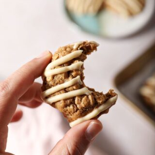 A bitten-into Oatmeal Cookie held in a hand above a stone surface with a plate of cookies