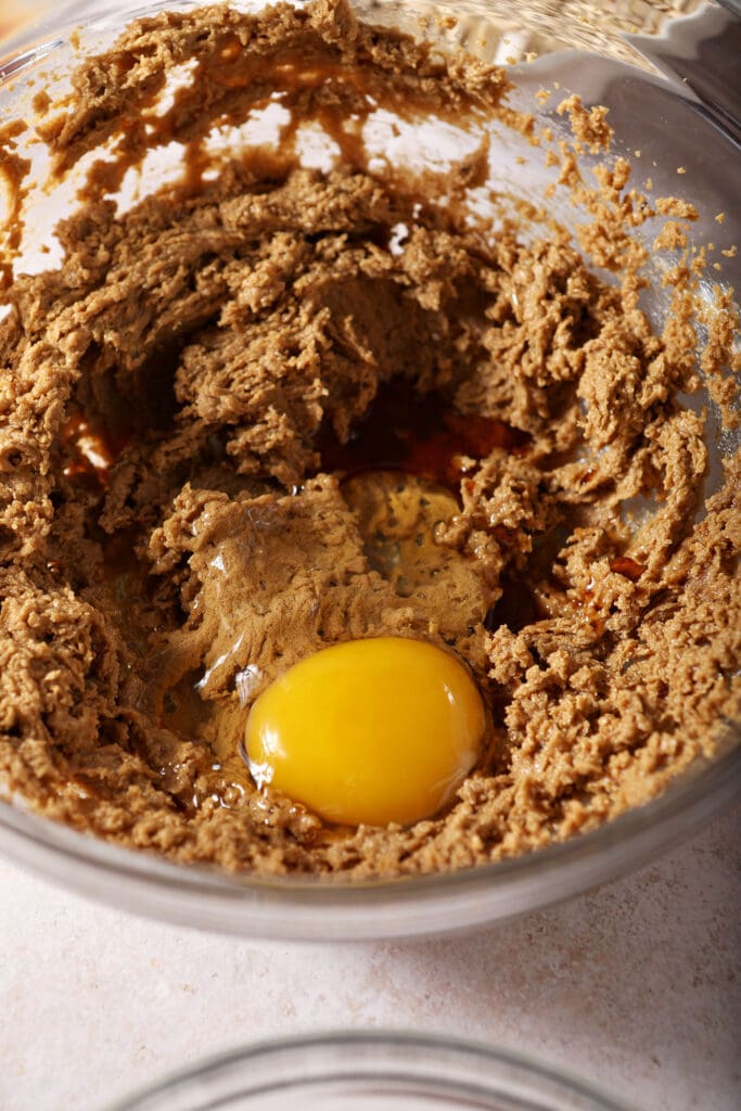 An egg and vanilla sit on top of creamed brown sugar and butter in a bowl