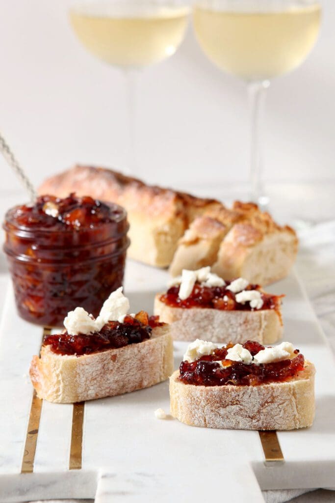 Close up of three slices of cranberry compote crostini in front of a jar of compote