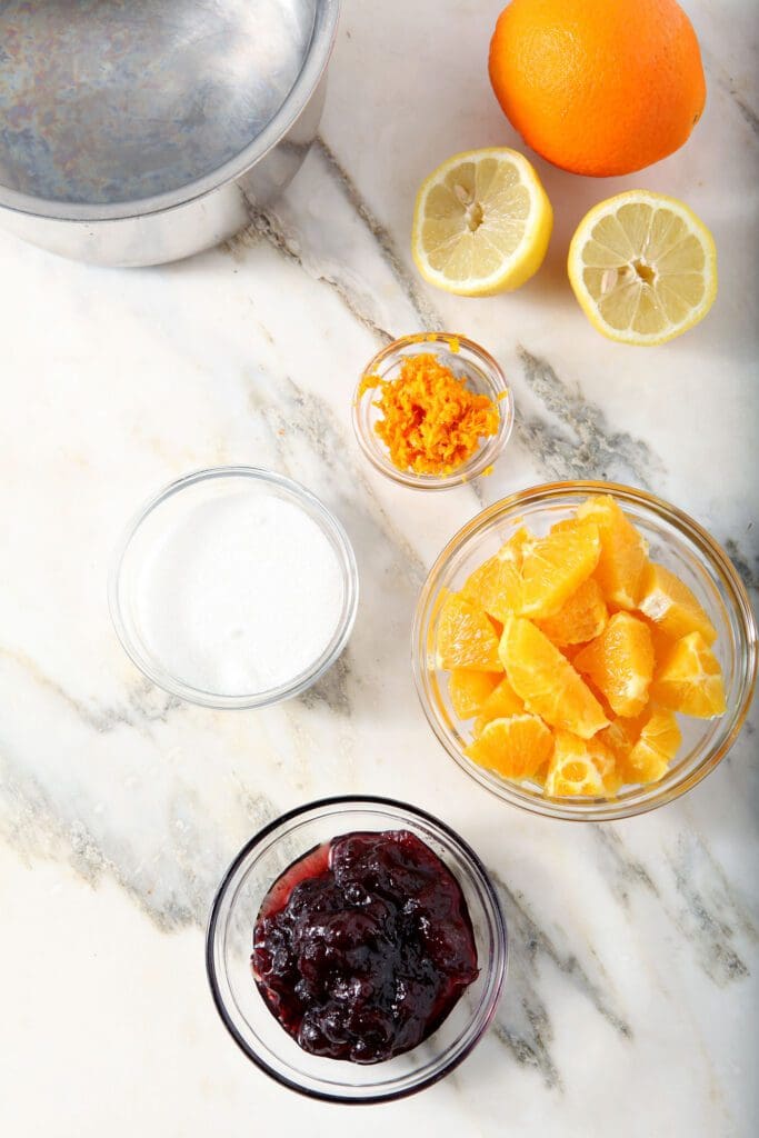 Ingredients to make cranberry compote in bowls on marble next to a saucepan