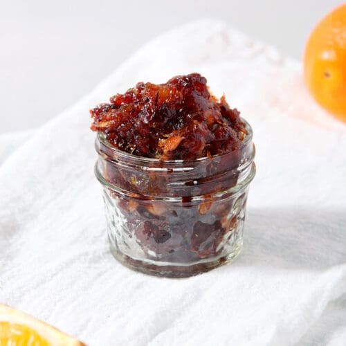 A jar of cranberry compote on a white linen towel next to orange slices