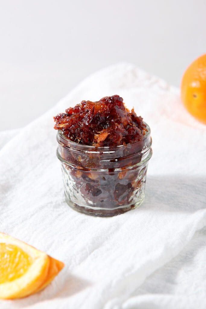 A jar of cranberry compote on a white linen towel next to orange slices