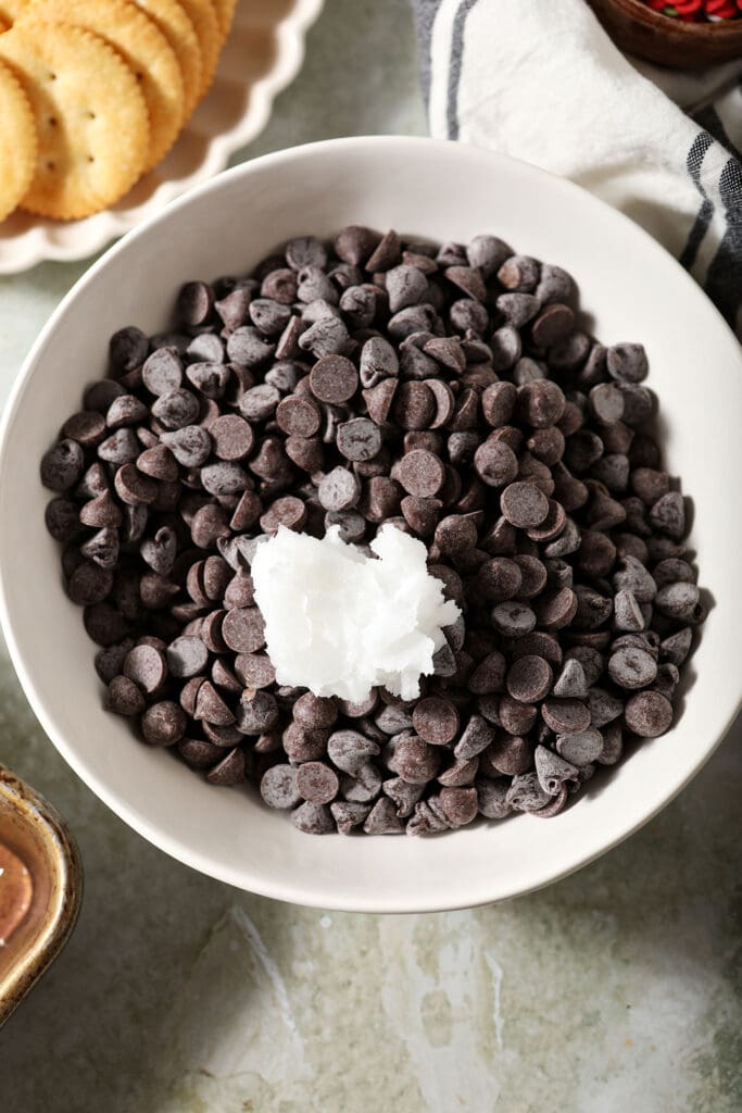 A bowl of chocolate chips with a dollop of solid coconut oil on top