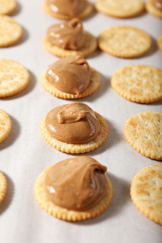 Ritz crackers with spoonfuls of peanut butter on top of half of them on a parchment-lined cookie sheet